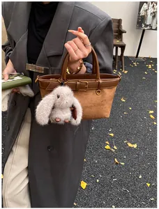 Détail d'un sac cabas marron mat avec un pendentif lapin en peluche gris et boucle métal