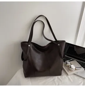 Detail of deep brown tote bag with lychee texture and metallic rivet accents on table