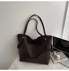 Detail of dark brown tote bag next to a laptop and headphones for commute