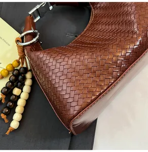 Close-up of woven brown leather bag featuring ethnic wood bead charm and silver hardware