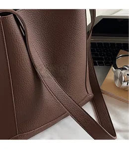 Detail of the litchi pattern leather texture and smooth shoulder strap on a brown bucket bag