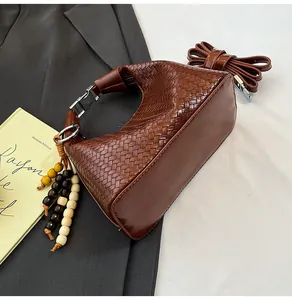 Detail of a brown woven hobo bag showing the wooden bead tassel and smooth leather texture