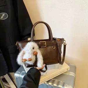Sac à main vintage marron mat avec breloque lapin en peluche sur une valise