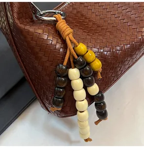 Close-up of dark brown woven leather texture with colorful wooden bead charm and silver ring zipper