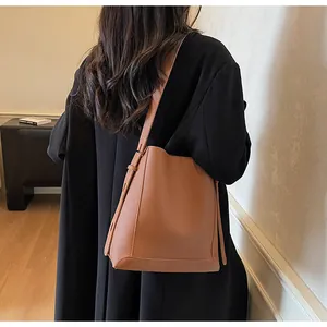 Detailed side view of a brown pebbled leather bucket bag worn as a shoulder strap bag