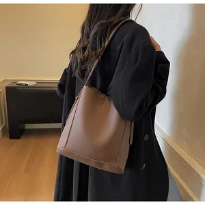 Detail of a brown lychee pattern leather bucket bag worn over the shoulder in a minimalist setting