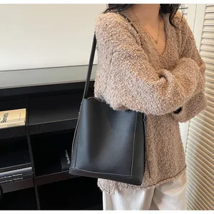 Black pebbled leather bucket bag styled with a brown knit sweater and white trousers