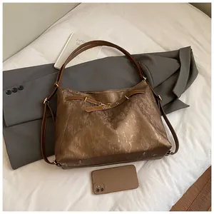 Detail of dark brown tote with glossy texture and buckle on a grey blazer