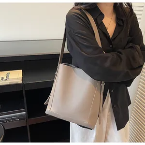 Taupe pebbled leather bucket bag shown as a crossbody with a minimalist indoor background