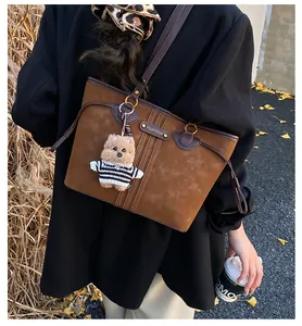 Gros plan sur un sac cabas en daim marron avec poignées en cuir et pendentif ourson