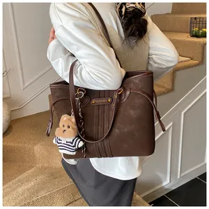 Détail d'un sac cabas marron foncé en daim avec un pendentif ours en peluche mignon