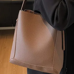 Minimalist dark brown lychee grain leather bucket bag shown on a model shoulder