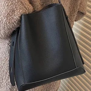 Minimalist black grained leather bucket bag with wide shoulder strap for casual daily commuting