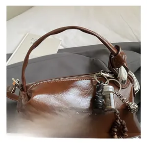 Detail of brown glossy leather Boston bag with knotted handle and decorative charms
