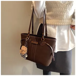 Détail d'un cabas en cuir marron foncé avec logo doré et breloque ours sur modèle