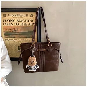 Détail d'un sac cabas vintage marron foncé avec un ourson en peluche et anneaux dorés