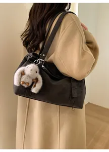 Détail latéral d'un grand sac cabas marron foncé avec pendentif lapin sur manteau beige