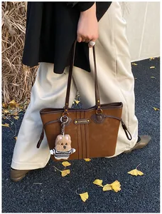 Détail d'un sac cabas en daim marron avec plaque logo en métal et breloque ours en peluche