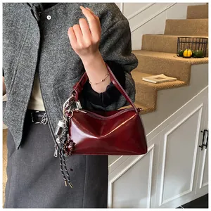 Detail shot of a dark red glossy leather handbag with ornate decorative charms and zipper