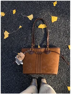 Gros plan d'un sac cabas en daim caramel avec bordures en cuir et petit ours en peluche