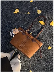 Détail du sac cabas en cuir mat marron foncé avec charm d'ours sur un sol d'automne pavé
