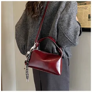 Detail of dark red glossy PU leather Boston bag worn crossbody with braided charm