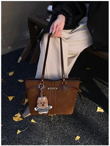 Sac cabas en daim marron avec anses en cuir et breloque chien dans un décor d'automne