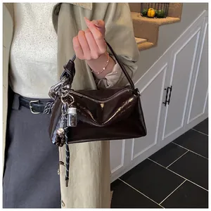 Detail of dark brown glossy pillow bag with knotted handle and fashion bag charms