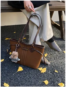 Sac fourre-tout marron avec ours peluche sur un banc entouré de feuilles d'automne