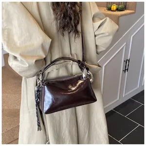 Detailed side view of dark brown glossy leather crossbody bag with silver hardware