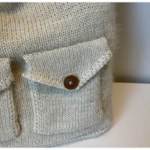 Vue détaillée du tricot crème de la veste avec une poche à rabat boutonnée