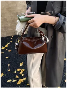 Brown patent leather satchel with silver zipper and chain detail held by a model