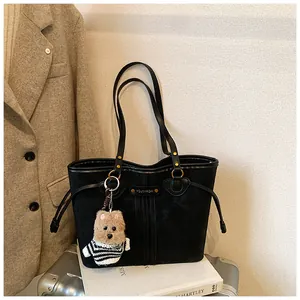 Détail d'un cabas noir en daim avec plaque logo dorée et pendentif chiot en peluche