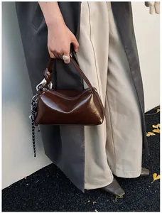 Detail of dark brown glossy leather handbag featuring unique knot handle and metal ring accents