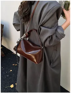 Deep brown oil-wax leather crossbody pillow bag shown on a model with grey coat