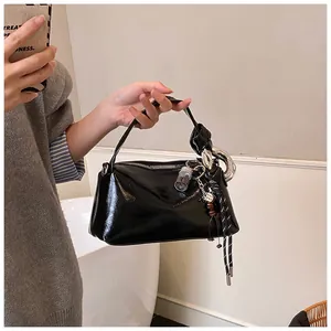 Detail of glossy black handbag featuring a knotted handle and decorative fringe charms
