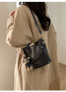 Close-up of dark brown bucket bag featuring gold buckle and houndstooth bunny charm