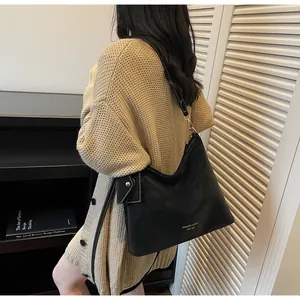 Detail of a black leather shoulder bag with white stitching and golden brand logo