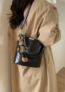 Detailed view of bucket bag with plaid rabbit charm and woven handle on trench coat