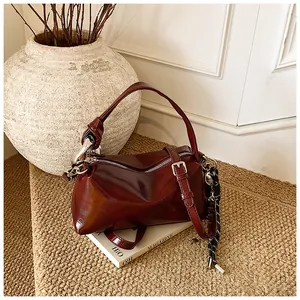 Close-up of a burgundy glossy leather tote bag with a silver zipper and decorative cord