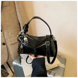 Detail of a black glossy pillow bag with stylish charms on a silver suitcase
