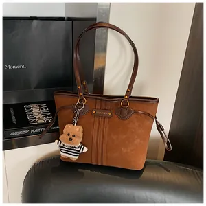 Détail du sac cabas en similicuir marron avec breloque ours en peluche et plaque métallique