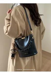 Detail of a black glossy bucket bag with golden lettering and a rabbit charm on a trench coat