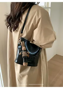 Detail of black glossy PU leather bucket bag with woven chain and rabbit doll charm