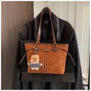 Détail d'un sac cabas en daim marron avec pendentif ours et logo métallique élégant