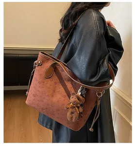 Brown embossed tote bag with cartoon dog pattern and plush bear charm on model shoulder