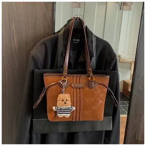 Détail d'un cabas en daim marron vintage avec garniture en cuir et pendentif ours mignon