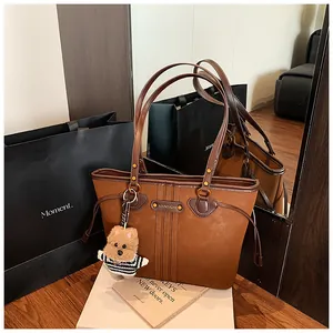 Gros plan d'un sac cabas marron avec poignées en cuir et breloque ours peluche