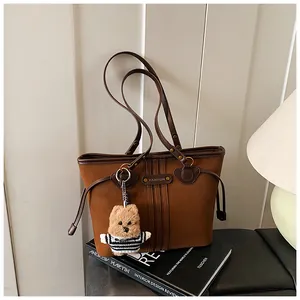 Détail d'un sac cabas en daim marron avec garniture en cuir et breloque d'ours