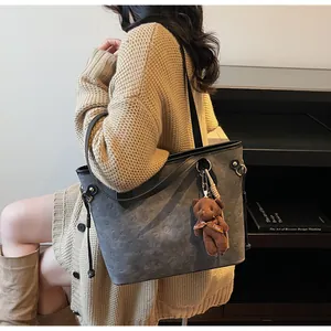 Detail of grey embossed tote bag with dark brown teddy bear charm and side drawstring